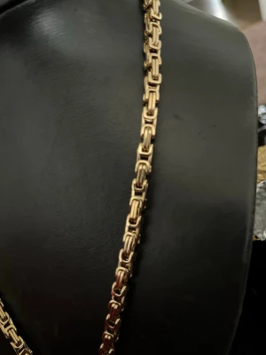 Guldfärgat kedjehalsband - Snyggt halsband i guldfärg med boxliknande kedjelänkar som ger ett robust och trendigt intryck. Halsbandet har en klassisk design utan hänge och passar perfekt för dig som gillar stilrena accessoarer. Materialet ser ut att vara metall med blank finish.