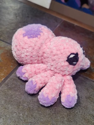 Rosa och lila virkad spindel - Söt handvirkad spindel i mjukt garn. Kroppen är ljusrosa med ett lila hjärta på ryggen och lila detaljer. Svarta broderade ögon ger ett gulligt uttryck. Perfekt som dekoration eller gosedjur.
