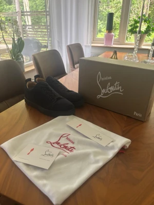 Svarta sneakers från Christian Louboutin - Stilrena svarta sneakers från Christian Louboutin med klassisk låg siluett och diskreta detaljer. Skorna har svart ovandel i mocka och matchande svarta skosnören. Kommer med originalkartong och dustbag.