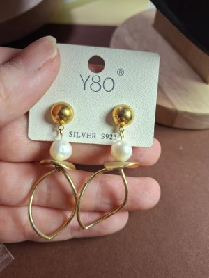 Guldörhängen med pärlor  - Snygga örhängen från Y80 i guldton med vita pärlor och unika, böjda ringar. Tillverkade i silver (S925) med guldfinish och dekorativa pärldetaljer som ger en elegant touch. Perfekta för dig som gillar trendiga accessoarer med lite extra stil.