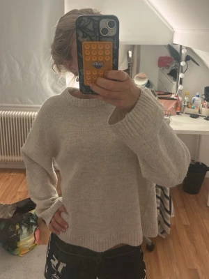 Beige oversized stickad tröja - Mysig beige stickad tröja med avslappnad passform och breda ribbade muddar vid ärmslut och hals. Perfekt för lager på lager och chill dagar. Tröjan har en enkel, stilren design utan synligt märke och är gjord i mjukt material.