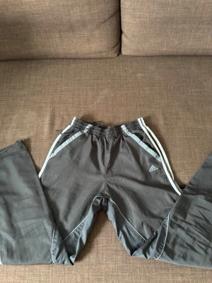Svart träningsbyxor från Adidas - Säljer ett par svarta träningsbyxor från Adidas med vita detaljer. Byxorna har resår i midjan och klassiska Adidas-ränder längs sidorna. Perfekta för gymmet eller löprundan.