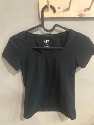 Svart kortärmad topp från 157 - En enkel och stilren svart topp från 157 med rund halsringning och korta ärmar. Tillverkad i mjuk bomull med lite elastan för extra stretch och bekväm passform. Perfekt basplagg att matcha med allt i garderoben.