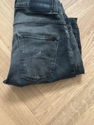 Svarta raka jeans från Lee - Säljer ett par svarta jeans från nudie med rak passform och klassiska bakfickor. Jeansen har en lätt tvättad look och är tillverkade i ett mjukt denimtyg som sitter skönt. Perfekta till en avslappnad stil och funkar året runt.