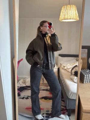 Mörkbrun skinnjacka med hög krage - Snygg mörkbrun skinnjacka med dragkedja framtill och hög krage. Jackan har en rak, boxig passform och resår i midjan. Två fickor framtill och stilren design som passar till många outfits.