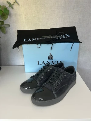 Svarta sneakers från Lanvin - Snygga svarta sneakers från Lanvin med ovandel i mocka och lackad tå. Skorna har svarta skosnören, metallfärgade öljetter och en klassisk låg siluett. Perfekta för dig som gillar stilrena och exklusiva detaljer. Allt og, uk 8 motsvarar 42/43