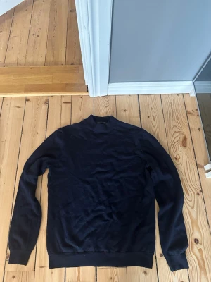 Mörkblå merinoulltröja H&M - Snygg mörkblå stickad tröja från H&M i mjuk merinoull. Tröjan har lång ärm, ribbade muddar och en klassisk rund hals. Perfekt för lager på lager och enkel att matcha med olika outfits.