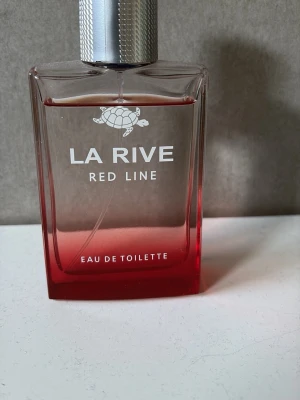 La Rive Red Line Eau de Toilette - La Rive Red Line Eau de Toilette i en rektangulär glasflaska med röd botten och silverfärgad kork. Flaskan har en stilren design med en vit sköldpadda på framsidan och tydlig text. Perfekt för dig som gillar fräscha och moderna dofter. Som man ser på bilden är den nästan helt full och doftar utmärkt på sommaren