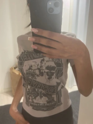Ljusgrå t-shirt med mörkgrå tryck - Säljer en ljusgrå t-shirt med ett stort mörkgrått grafiskt tryck framtill. T-shirten har klassisk passform och korta ärmar. Perfekt för dig som gillar statement-plagg med coolt motiv.