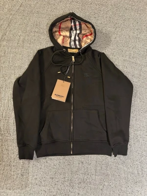 Svart hoodie från Burberry - En svart burberry hoodie med prislapp på, storlek M men sitter mer som S då den är väldigt liten i storleken. Hör gärna av dig om du har frågor eller funderingar. 