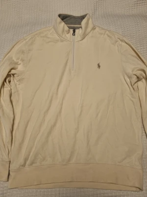 Beige halfzip från Polo Ralph Lauren - Snygg beige långärmad tröja från Polo Ralph Lauren med halv dragkedja och broderad logga på bröstet. Insidan av kragen är grå och mjuk. Perfekt för lager-på-lager och enkel att matcha med jeans eller chinos. 