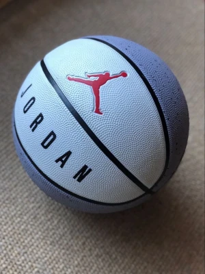 Jordan basketboll vit och grå - Säljer en basketboll från Jordan i vit och grå färg med svarta linjer och det klassiska röda Jumpman-logotypen. Bollen har en greppvänlig yta och tydlig text med JORDAN tryckt på sidan. Perfekt för basketträning eller spel med vänner.