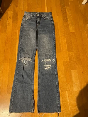 Pull&Bear 34 jeans med slitningar - Säljer ett par fina  blå raka jeans med slitna detaljer över knäna och råa, fransiga benslut. Märke: Pull &Bear, storlek 34.