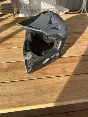 Grå motocrosshjälm från Raven - Säljer en grå motocrosshjälm från Raven med svart och silverfärgade detaljer. Hjälmen har en skärm framtill och ventiler för bra luftflöde. Invändigt finns mjuk vaddering för extra komfort. Hjälmen har en del skrapmärken från att ha legat på backen men inget som påverkar dess skydd. Nypris är cirka 2100 kronor, skriv om du har frågor eller önskar mer bilder. 