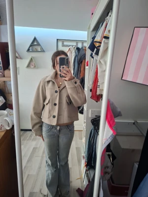 Beige jacka/kapa - Säljer en jätte fin beige jacka med svarta knappar och krage. Jackan har en loose passform och långa ärmar. Enkel och stilren design som passar till många outfits. Säljer eftersom har för många jackor. Använd ändast nån gång.
