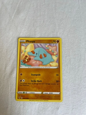 Phanpy Pokémonkort - Säljer ett Phanpy Pokémonkort med gul ram och färgglad illustration av Phanpy på framsidan. Kortet har attackerna Stampede och Strike Back samt tydliga symboler för svaghet och motstånd. Baksidan har klassiskt blått Pokémon-motiv.
