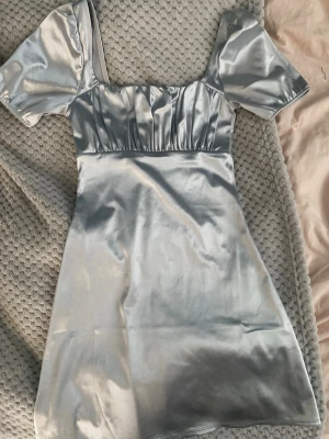 Silvrig kort klänning - Supersnygg silvrig kort klänning i satinliknande material med puffärmar och fyrkantig urringning. Den är köpt på Plick och tror att den först är från HM