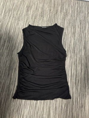 Svart ärmlös topp från Stradivarius - Säljer en svart, ärmlös topp från Stradivarius. Modellen är slim och har en enkel, stilren design med rund halsringning. Tyvärr har den blivit förliten! 