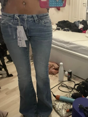 Ljusblå bootcut jeans från gina  - Säljer ett par ljusblå bootcut jeans från gina  med klassisk femficksdesign och normal midja. Jeansen har en snygg tvätt och utsvängda ben, perfekta för en trendig look. Materialet är mjukt och stretchigt för extra komfort. De är helt nya, aldrig använts! 