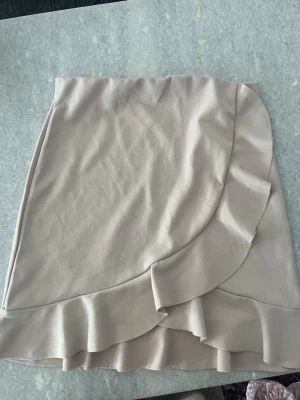 Beige rosa kjol med volanger - Supersöt beige rosa kjol med volangkant. Kjolen har en mjuk och lätt material som ger en skön känsla och snygg passform. Perfekt att styla med en enkel topp eller stickad tröja. Perfekt för sommaren💕