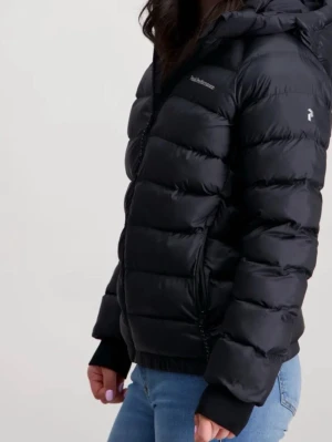 Svart dunjacka från Peak Performance - Snygg svart dunjacka från Peak Performance med huva och dragkedja framtill. Jackan har en puffig design, två sidofickor med dragkedja och diskret logga på bröstet och ärmen. Perfekt för kalla vinterdagar och riktigt varm tack vare dunfyllningen.