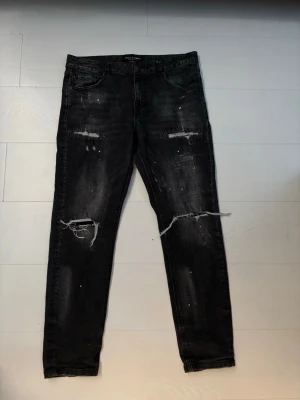 Svarta ripped jeans Supply & Demand. Pris kan diskuteras - Snygga svarta jeans från Supply & Demand med slitna detaljer och hål på knäna. Jeansen har en smal passform och coola slitningar samt färgstänk för en trendig look. Perfekta för dig som gillar streetstyle och vill sticka ut.