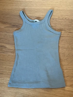 Ljusgrönt ribbat linne - Säljer ett ljusgrönt ribbat linne med smala axelband och rundad halsringning. Toppen är ärmlös och har en slim passform som sitter snyggt på kroppen. Perfekt att styla med jeans eller kjol för en enkel och fräsch look.