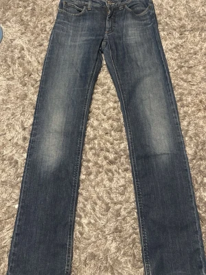 Acne studio jeans - Säljer ett par klassiska blå jeans med raka ben och diskreta slitningar på framsidan. Jeansen har fem fickor och en knappgylf. Materialet är denim och färgen är mörkblå med ljusare partier. Perfekt för dig som gillar en tidlös och avslappnad look.