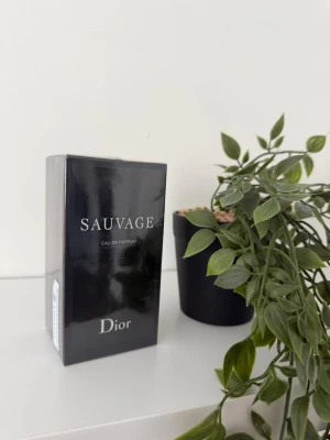 Dior Sauvage Eau de Parfum - Helt ny oöppnad Dior Sauvage Eau de Parfum i en elegant, svart rektangulär kartong med silverfärgad text. Parfymen är känd för sin fräscha och kryddiga doftprofil och passar dig som vill ha en modern och exklusiv parfym. Perfekt som present eller till dig själv.