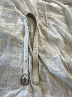 Vitt skärp i skinn med silverfärgat spänne - Snyggt vitt skärp i skinn med ett klassiskt silverfärgat spänne. Skärpet har dekorativa sömmar längs hela längden och kan spännande vid många hål. Har en del missfärgningar