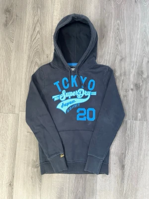 Mörkblå Superdry hoodie Tokyo print - Snygg svart hoodie från Superdry med stor             blå/ljusblå Tokyo-print och logga på bröstet🤩 Passar S och Xs🤗 Hör av er vid funderingar samt snabbaffär😇