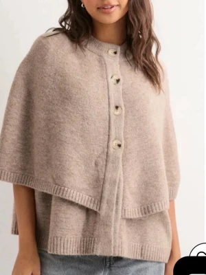 Stickad poncho med knappar - Säljer en beige/brun stickad poncho med stora knappar framtill och ribbade kanter. 💌Storlek S, och i nytt skick. (En liten maska som går att fixa men värd att nämna).💕