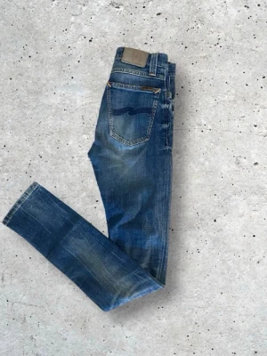 Blå jeans från Nudie Jeans - Snygga blå jeans från Nudie Jeans med klassisk femficksdesign och najs tväyy. Jeansen har raka ben och en mörkblå tvätt med ljusare partier. Pris kan diskuteras.                     Man får om man vill med ett par till nudies. Mer info privat!