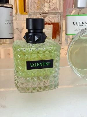 Valentino parfym grön glasflaska - Säljer en lyxig parfym från Valentino i en snygg grön glasflaska med rutmönster och svart etikett. Flaskan har en cool svart kork med nitar som ger en edgy känsla. Perfekt för dig som vill ha en unik och trendig doft på hyllan.