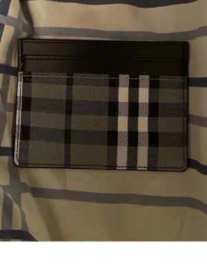 Burberry rutigt kortfodral svart/grå - Snyggt kortfodral från Burberry i svart och grått med klassiskt rutmönster. Fodralet har flera kortfack och är tillverkat i slätt läder med tryckt mönster. Perfekt för dig som vill ha en stilren och lyxig accessoar i fickan.