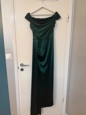 Balklänning - Elegant mörkgrön långklänning i glansigt material med axelbandslös design och draperad överdel. Perfekt för speciella tillfällen där du vill sticka ut med en stilren look.