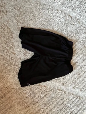 Svarta träningsshorts från SOC - Säljer ett par svarta träningsshorts från SOC med elastisk midja. Perfekta för gymmet eller löpning, tillverkade i lätt och bekvämt syntetmaterial som andas. Diskret logga på benet och enkel design som passar till allt.