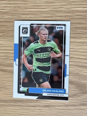 Panini fotbollskort Erling Haaland - Säljer ett Panini Donruss Optic fotbollskort med Erling Haaland från Manchester City. Kortet har en färgstark design med Haaland i grön och svart matchtröja. Perfekt för samlare av fotbollskort och fans av Premier League.