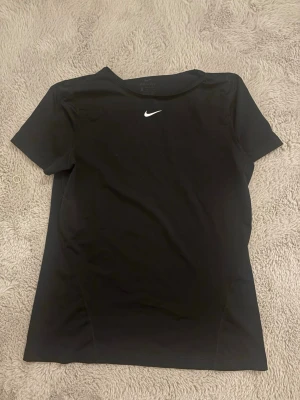 Svart Nike t-shirt med logga - Snygg svart t-shirt från Nike med klassisk vit logga på bröstet. Tillverkad i ett mjukt och stretchigt funktionsmaterial som passar perfekt till träning eller sportaktiviteter. T-shirten har rund halsringning och korta ärmar. Använd men fint skick 