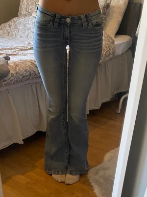 Blå bootcut jeans med broderade fickor - Snygga blå bootcut jeans med lätt slitning och broderade bakfickor. Jeansen har klassisk femficksdesign, låg midja och stängs med knapp och dragkedja. Perfekta för en avslappnad och trendig look.