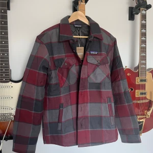 Jacka från Patagonia - Fodrad overshirt från Patagonia i röd och grå rutig design. Storlek S, men funkar S/M. Nypris ligger på över 2000kr. Helt ny, skriv vid frågor! 