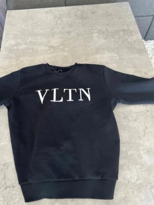 Svart sweatshirt från Valentino - Cool svart sweatshirt från Valentino med VLTN-tryck i vitt på bröstet. Tröjan har rund hals, ribbade muddar och är tillverkad i mjukt material som passar perfekt till en avslappnad stil.