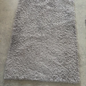 Ljusgrå fluffig matta - Säljer en rektangulär ljusgrå matta med lång lugg och mjuk, fluffig känsla. Perfekt för att skapa en mysig känsla i rummet och passar bra på både sovrumsgolv och vardagsrumsgolv. Mattan har en neutral färg som är lätt att matcha med annan inredning.