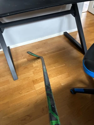 Svart och grön innebandyklubba - Säljer en innebandyklubba med svart grundfärg och gröna detaljer. Klubban har ett böjt blad och ett mönstrat skaft. Perfekt för dig som gillar innebandy och vill ha en snygg klubba med cool design.