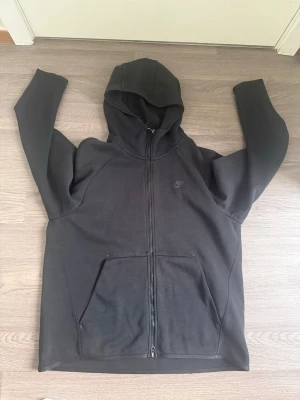 Svart zip hoodie från Nike old season - Säljer en svart  Nike tech old season  med dragkedja framtill och två stora fickor. Klassisk design med diskret Nike-logga på bröstet och huva. Tillverkad i mjukt material som passar perfekt till chill eller streetwear.