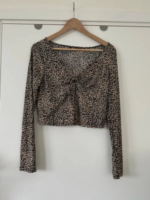 Leopardmönstrad topp, storlek L/XL - Gullig topp / tröja med leopardmönster och långa ärmar. Toppen har en knutdetalj framtill som skapar en smickrande rynkad effekt. Den har en rundad halsringning och i mjukt elastiskt tyg. Storlek 40/42/L/XL. Mycket fint skick, som ny!  Skickas mot porto, kan även hämtas i Stockholm. 