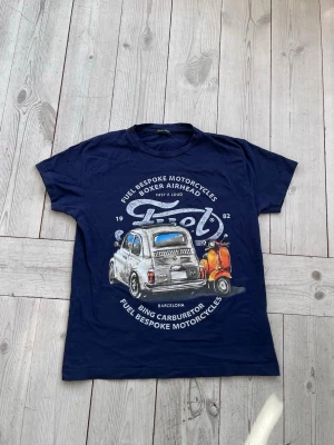 T-shirt från italien med snyggt tryck - Mörkblå t-shirt med coolt tryck av en retrobil och text på framsidan. Tillverkad i Italien och i mjuk bomull. Klassisk passform med korta ärmar, perfekt för sommaren. Storlek S men mindre i passformen.