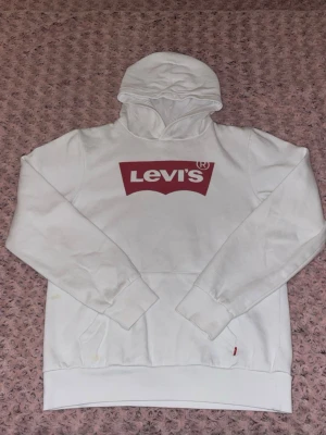Levi’s hoodie - Säljer en vit hoodie från Levi's med  röd logga på bröstet. Perfekt för en avslappnad och trendig stil. Hoodie har lite små fläckar (se bilder) men vad andra har sagt till mig så märks dom inte så mycket, bara när man nämner och visar 🤍