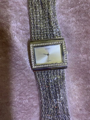 Cussi klocka med glittrig länk - Snygg rektangulär klocka från Cussi med glittrande stenar runt urtavlan och bred metallänk. Finns i både silver och guld. Urtavlan är stilren och ljus, och länken består av flera tunna kedjor som ger en exklusiv känsla. 359kr/st 