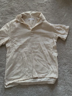 Beige henley-skjorta från Zara - Säljer en beige henley-skjorta från Zara i linne. Skjortan har korta ärmar, klassisk krage och knappar vid halsen. Perfekt för en avslappnad och stilren look. Passar dig som gillar enkla och svala plagg.